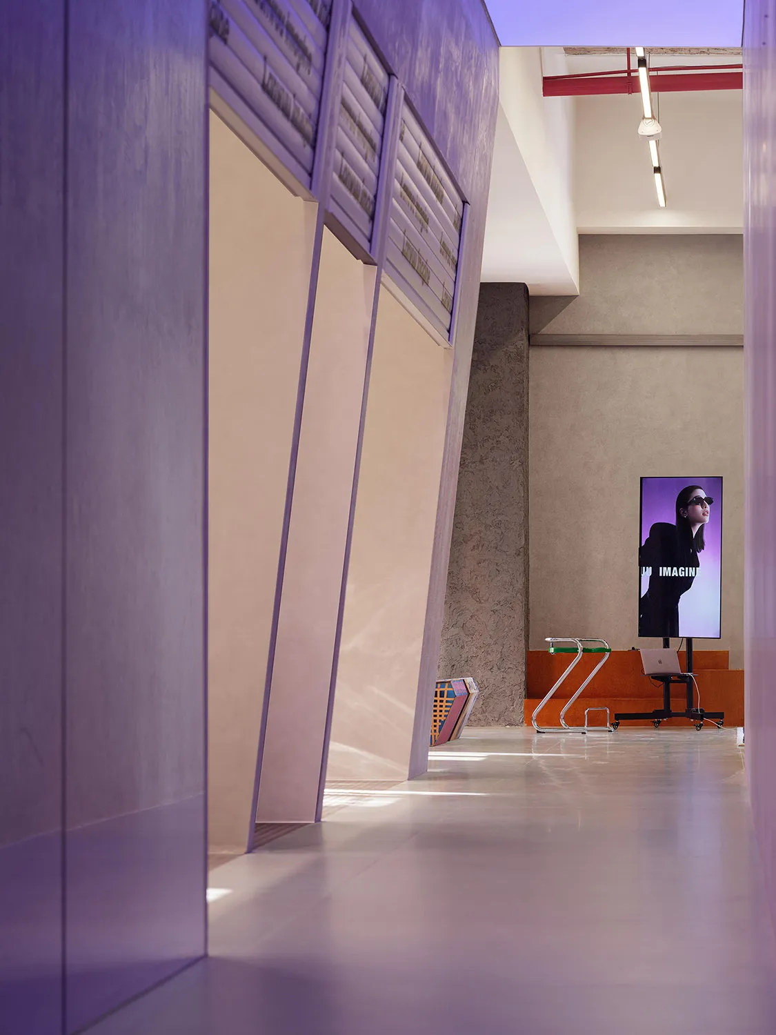 A modern lobby with concrete walls, floors, and ceiling, featuring a digital screen displaying a woman in sunglasses.