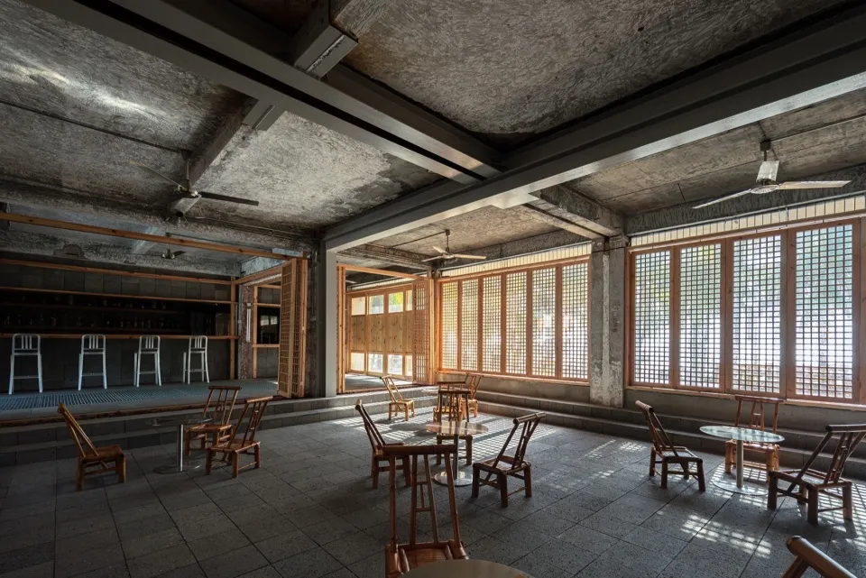 Industrial-style restaurant bar with concrete walls, wooden furniture, and large windows.