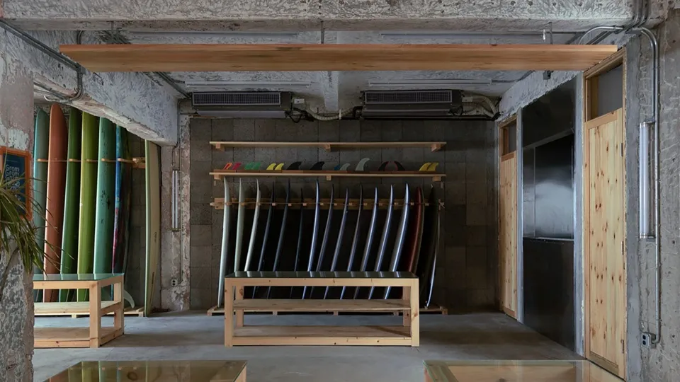 A minimalist indoor surf shop with wooden racks and concrete walls.