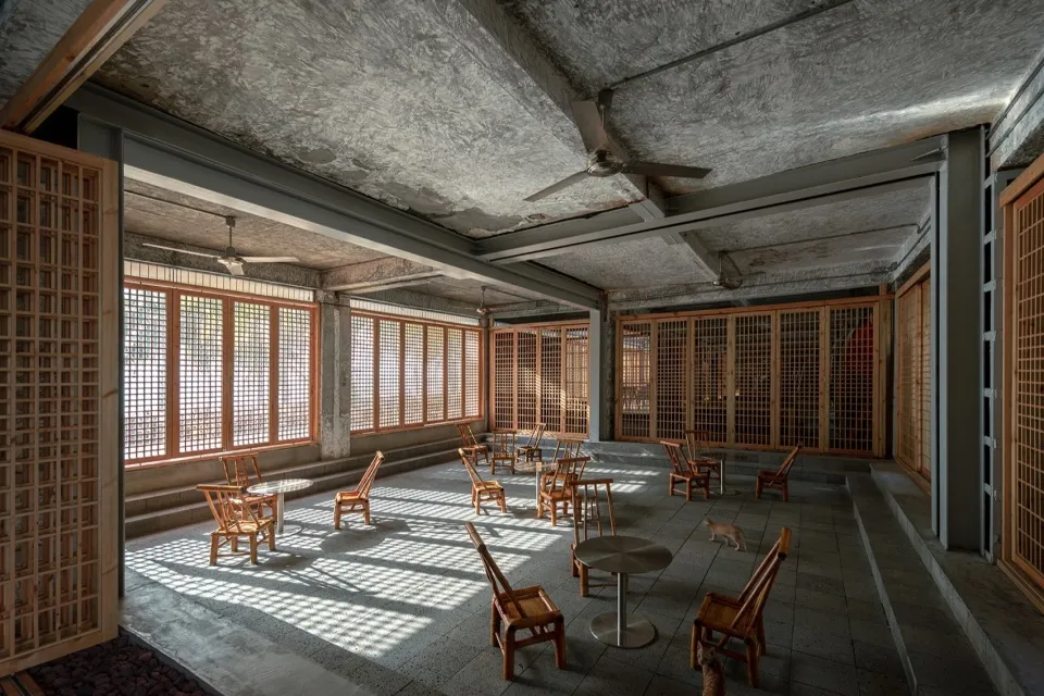 A minimalist coffee shop interior made of concrete material, with wooden furniture and large windows allowing natural light.