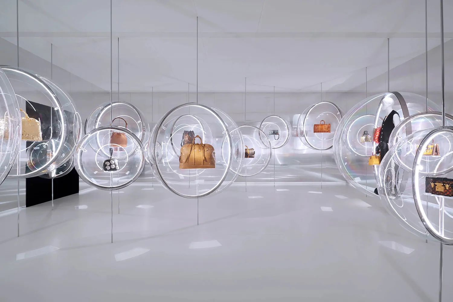 A minimalist retail display featuring glass spheres containing handbags.
