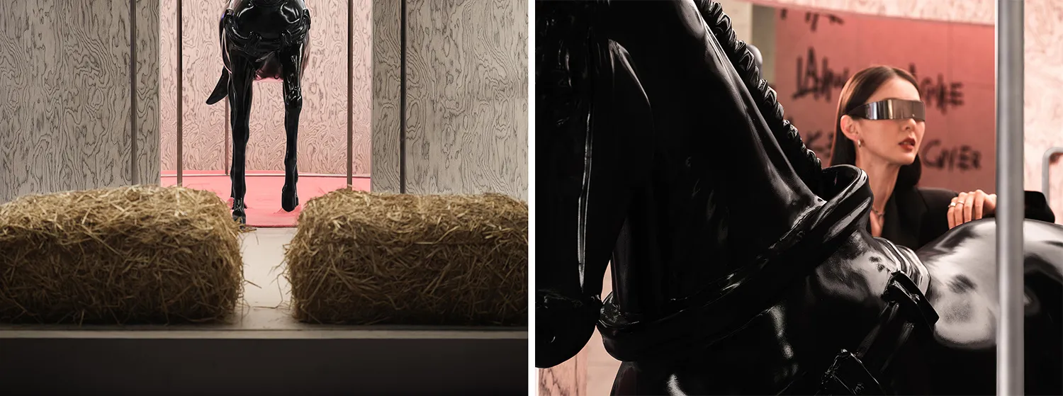 A photograph of a black plastic horse standing on a pink surface surrounded by hay bales in a barn setting.
