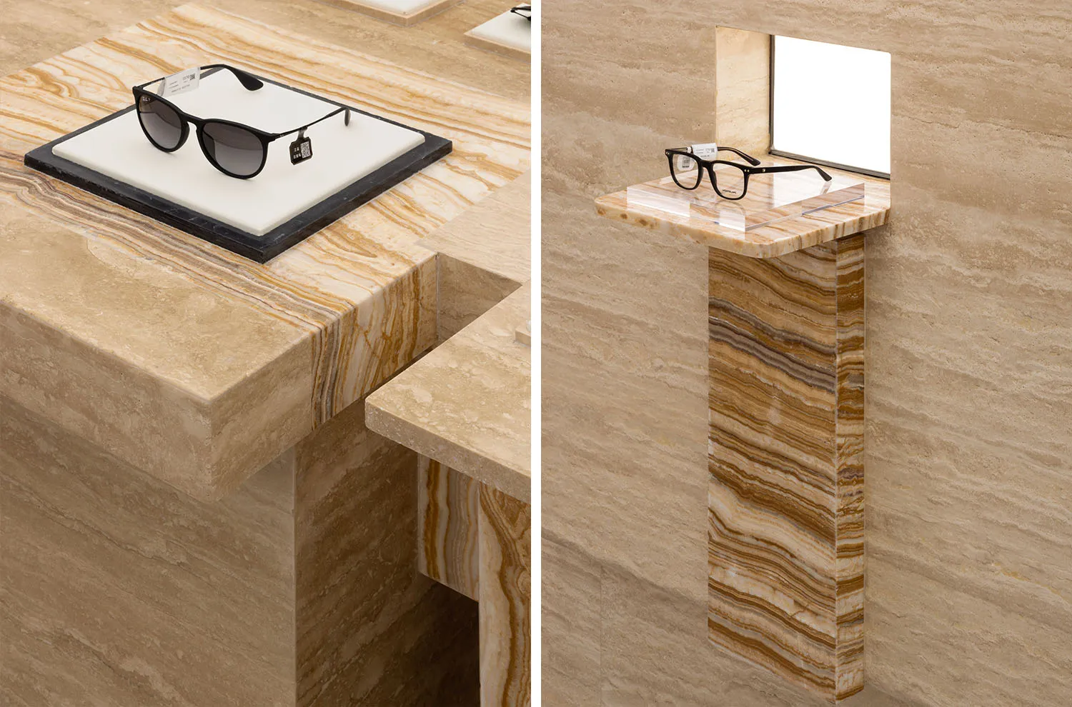 A stylish retail display featuring black sunglasses and a clear spectacle frame placed on a marble surface and pedestal.