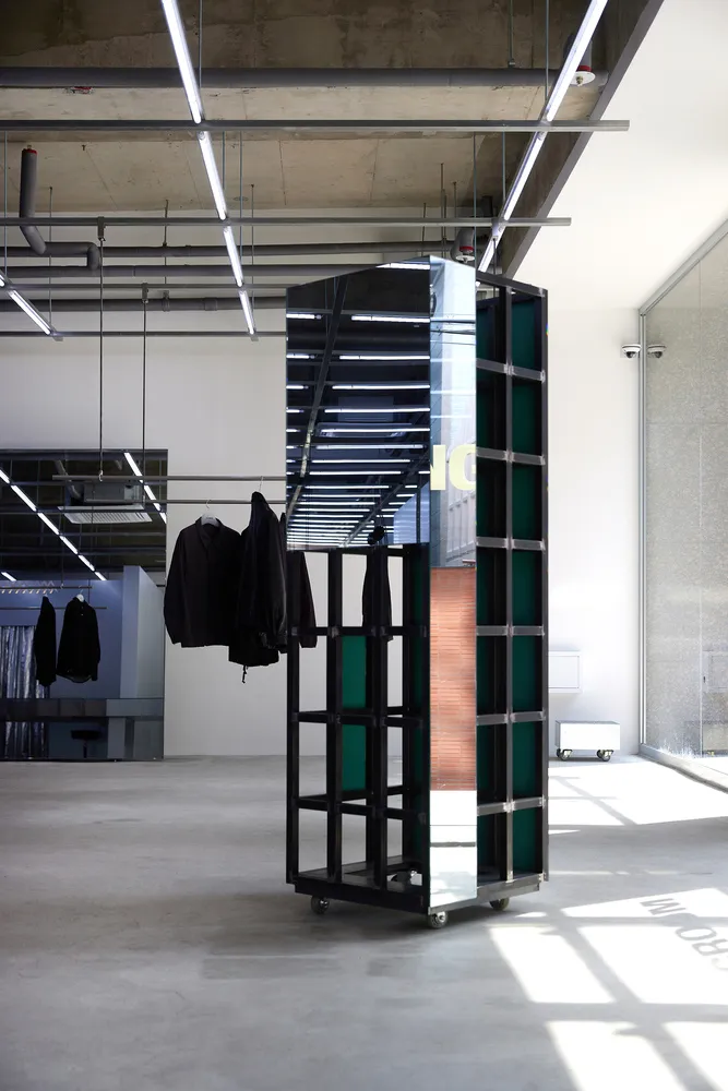 A modern metal clothing display system with wheels, placed in an empty interior space with a concrete floor and visible pipes