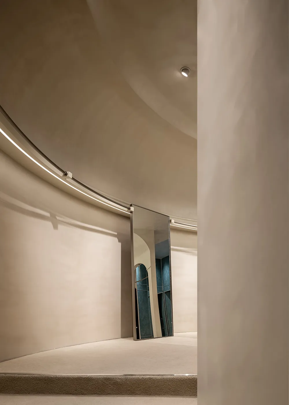 A modern interior space with curved walls and neutral materials, including a reflective mirror.