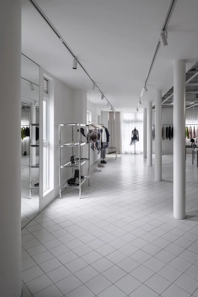 A minimalist retail store with white porcelain floors and white walls showcasing clothing on racks and mannequins.