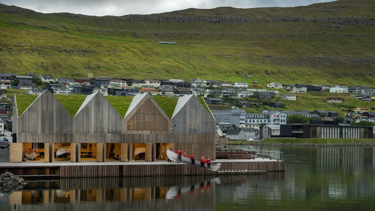 Modern wooden architectural design with a grass-covered hillside in the background.