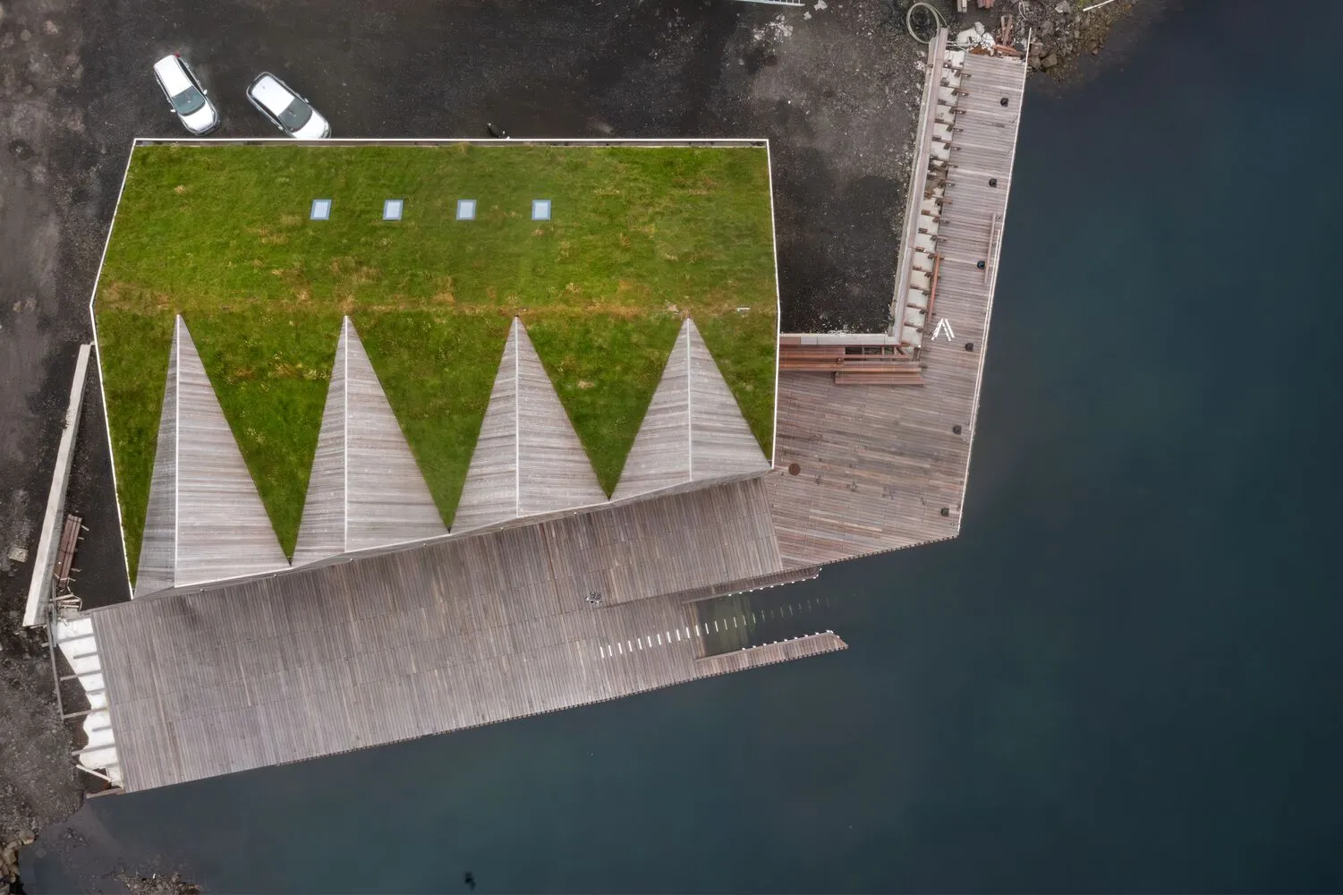 Modern boat bunker with a green-topped roof and wooden deck next to a body of water.