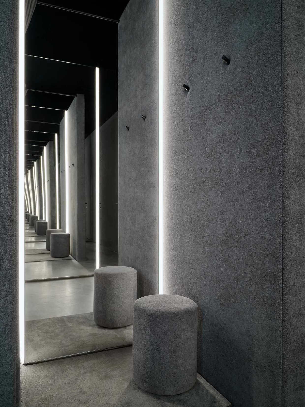 A minimalist interior design space featuring a concrete bar counter, with sleek, linear lighting fixtures and cushioned stool