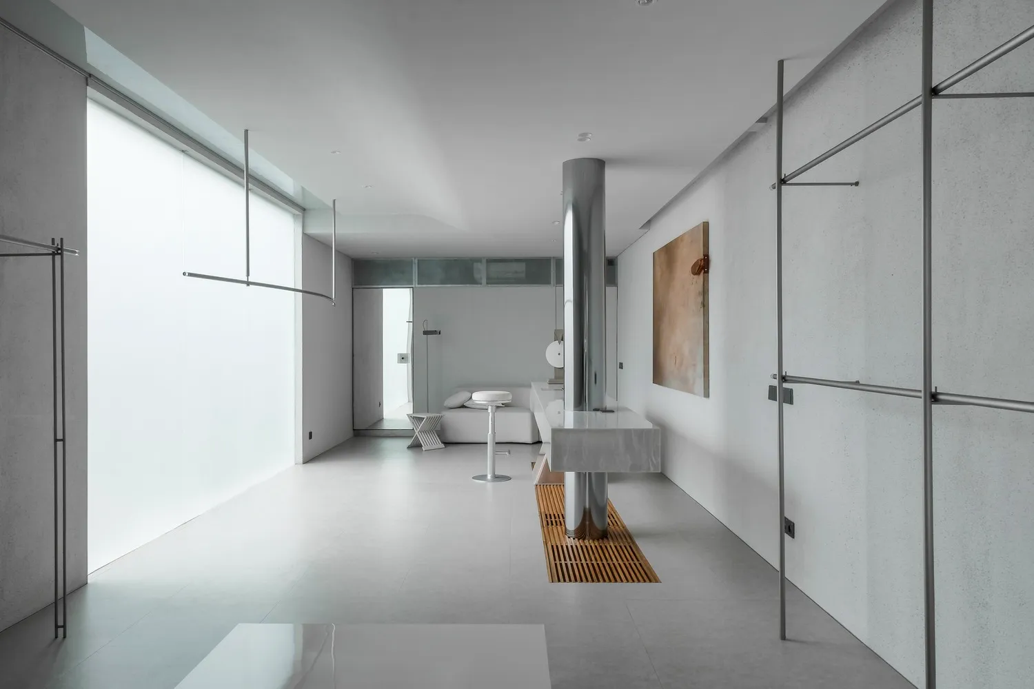 A minimalist living room with concrete walls, metal accents, and a glass column.