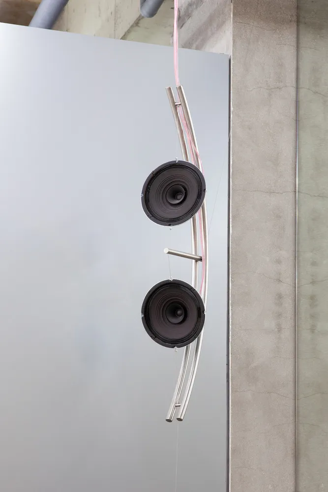 Two black sound speakers mounted on a metal frame in a minimalistic environment.