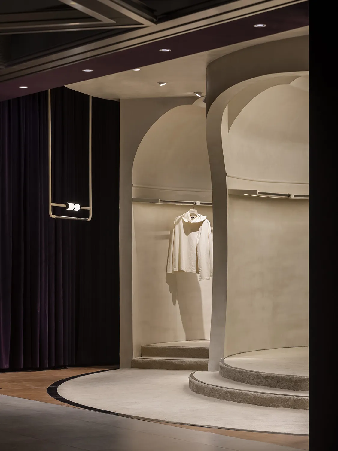 A minimalist retail display featuring a white garment on a concrete platform with a purple curtain backdrop.