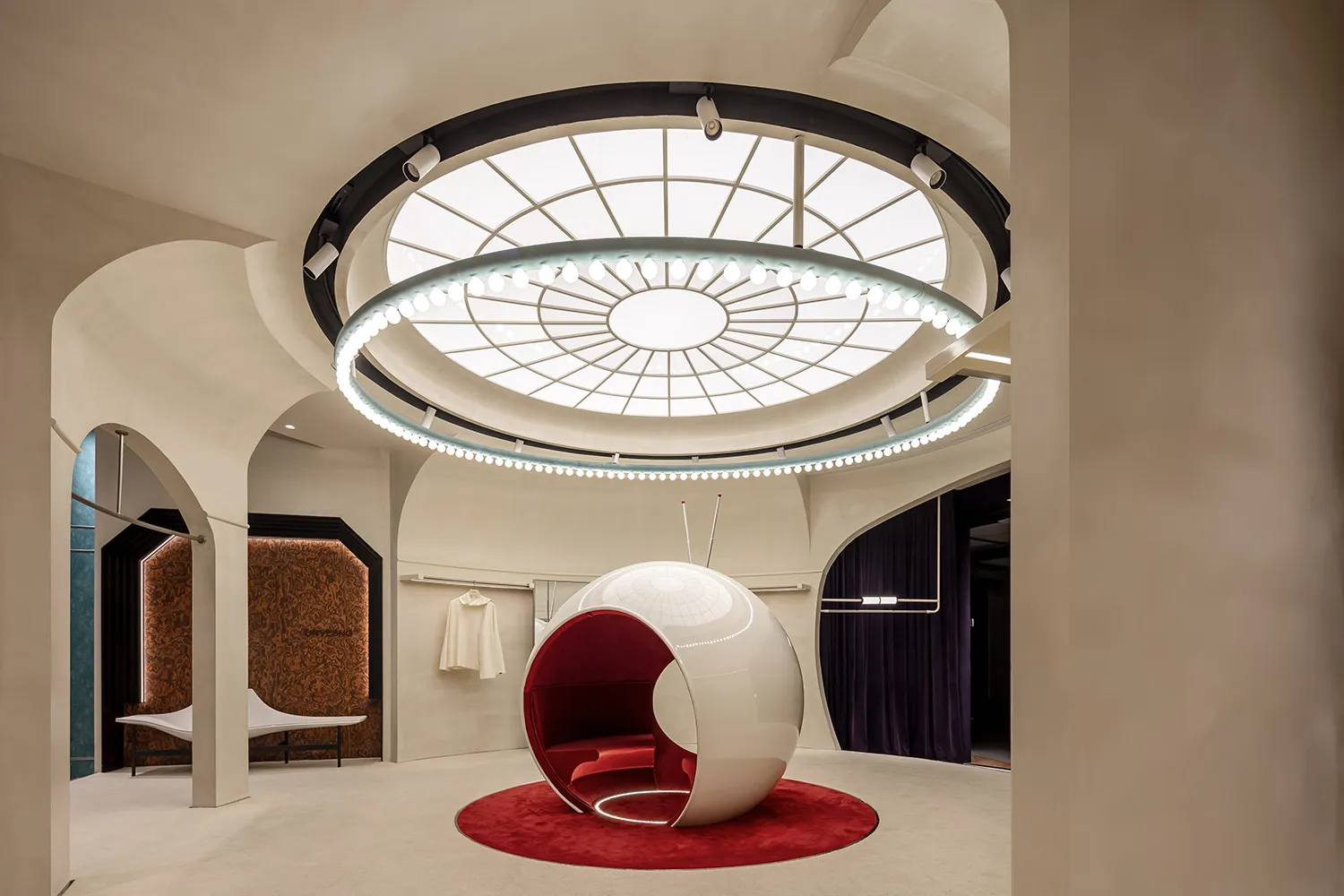 Modern retail shop interior featuring a circular glass space with a white and red circular pod on a red carpet.
