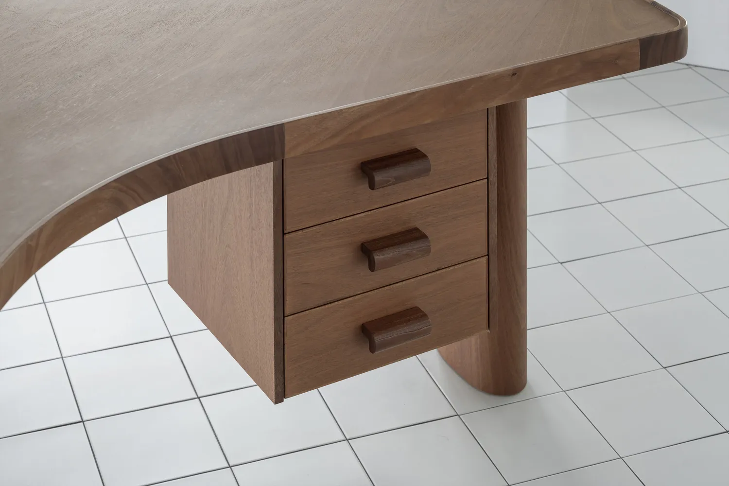 A modern wooden desk with curved edges and three drawers.