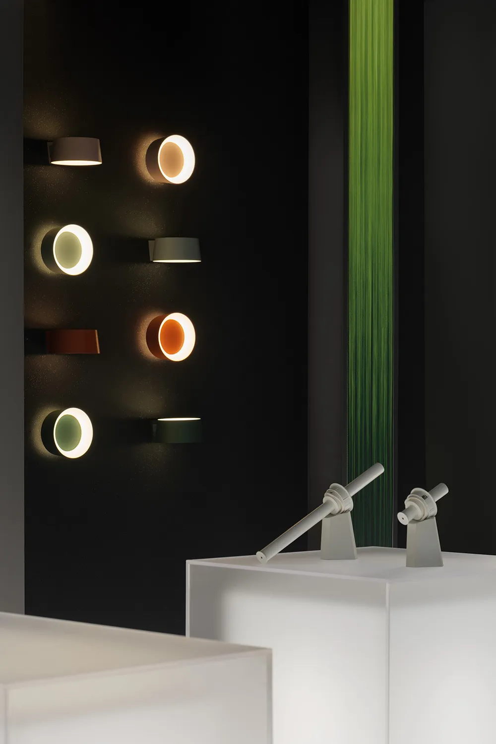 Multiple metal wall-mounted lights of varying colors displayed on a black wall.
