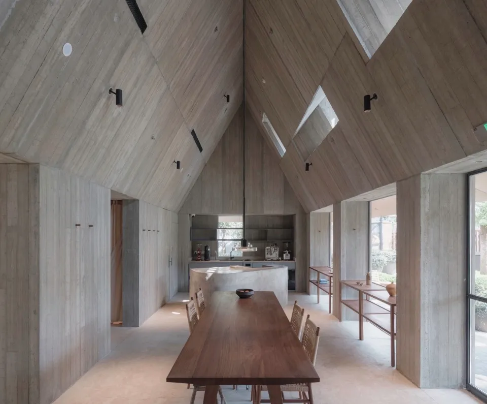 極簡住宅廚房，裸露混凝土牆面與天花板，搭配大型木製餐桌與餐椅。
