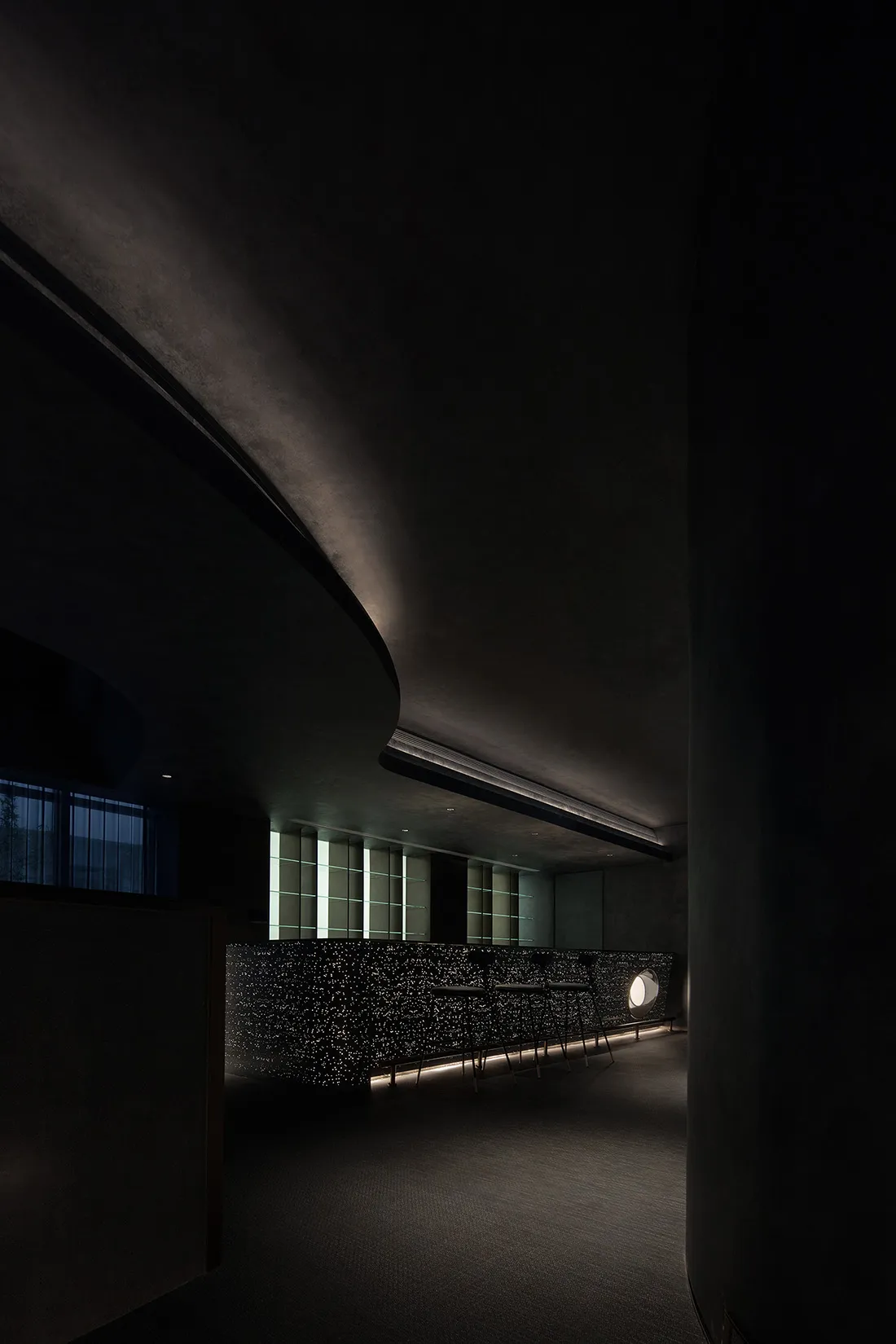 A minimalist modern cafe bar featuring a sleek concrete tile bar counter with integrated lighting and a unique circular table