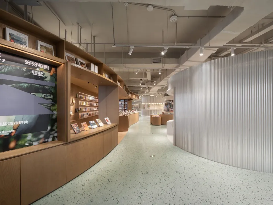 A spacious, modern bookstore interior with wooden shelves and concrete flooring.
