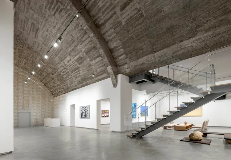 Modern museum exhibition space featuring a concrete ceiling and stairs.