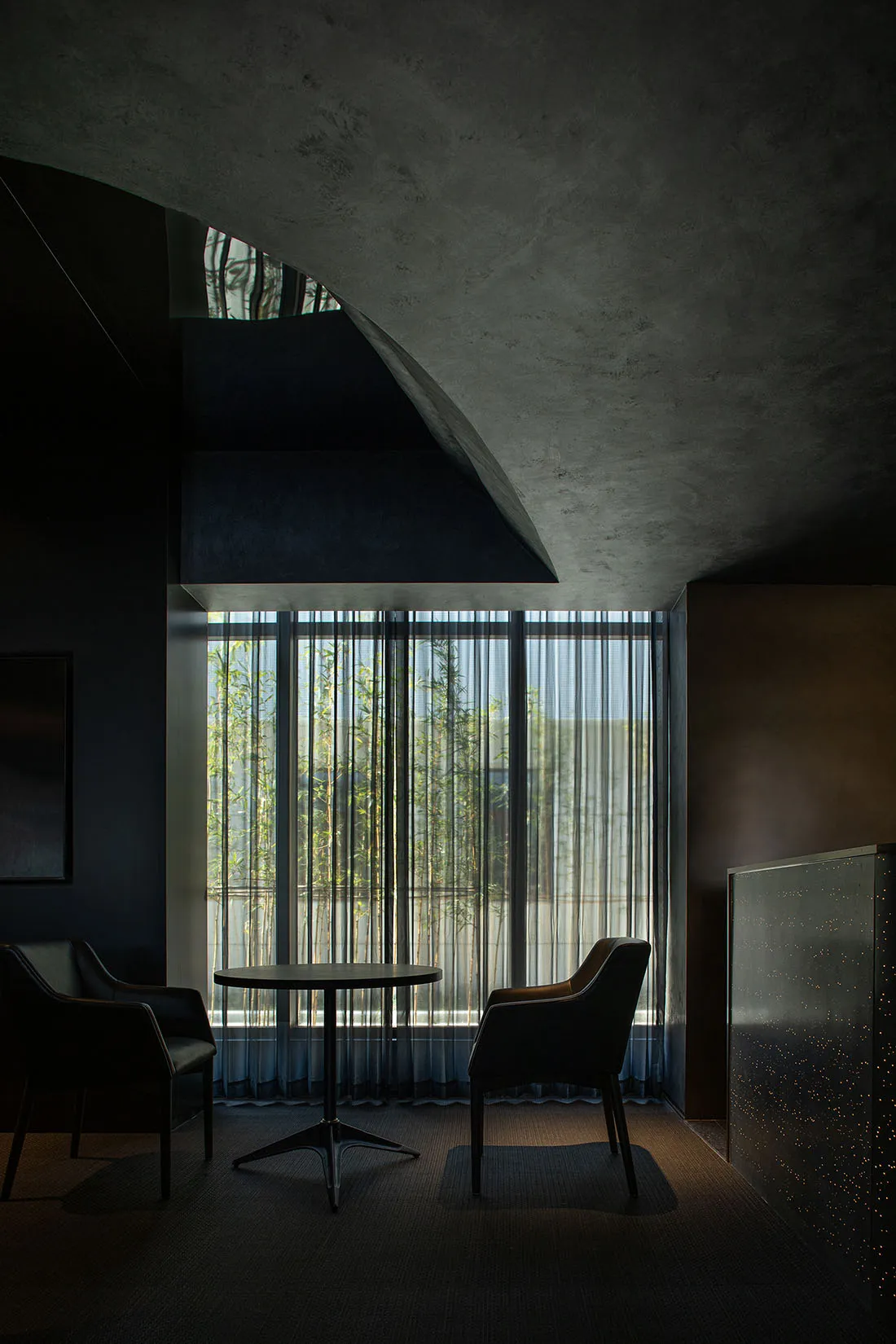 Industrial-style lobby with minimalist design and concrete materials, featuring a round table and two chairs.