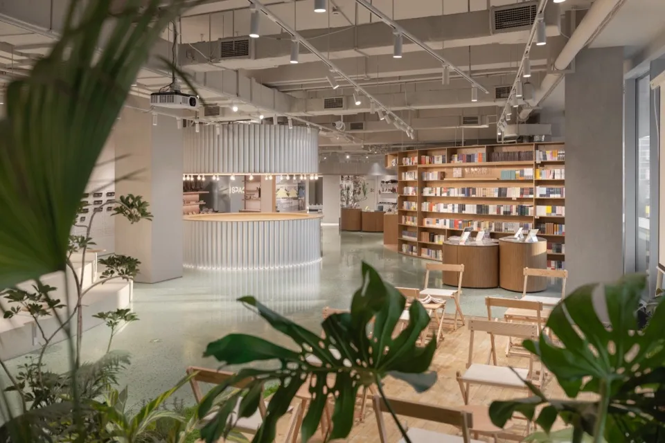 現代咖啡廳休息區,混凝土地板搭配木質家具,點綴綠色植物與中央圓形吧台。