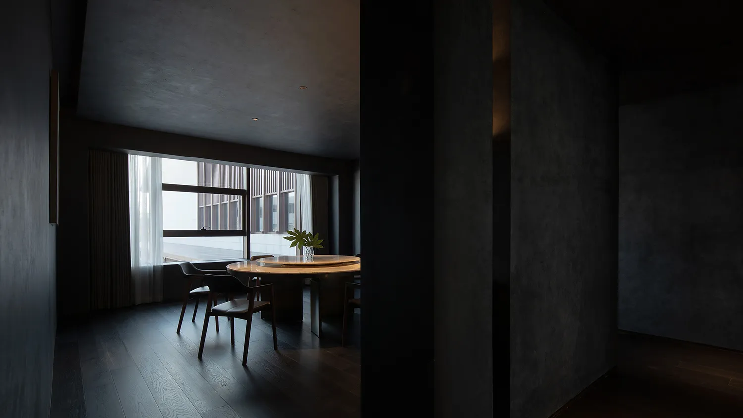 Interior photograph of a modern dark dining room with dark wood flooring and a round table.
