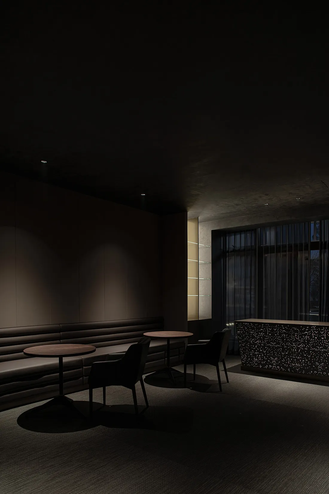 A sleek, dark-themed hotel lounge with modern furniture and dark stone finishes.