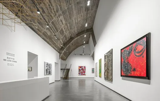 Modern industrial art gallery with concrete walls and steel beams, featuring various art pieces on the walls.