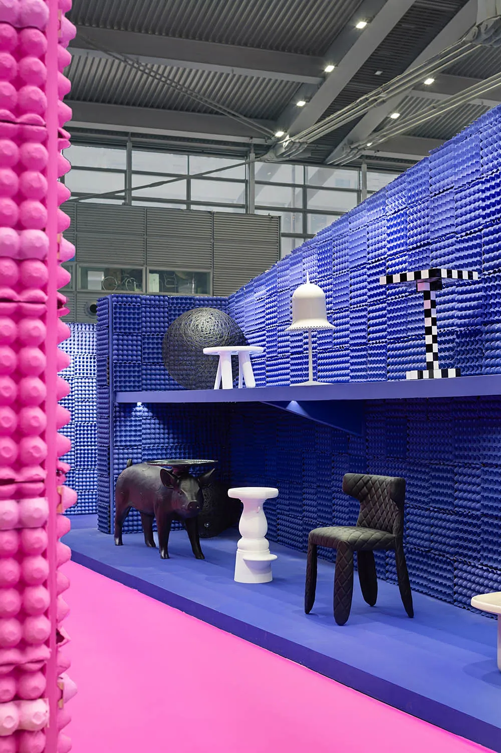 Exhibition display featuring plastic egg crate wall and various furniture elements.