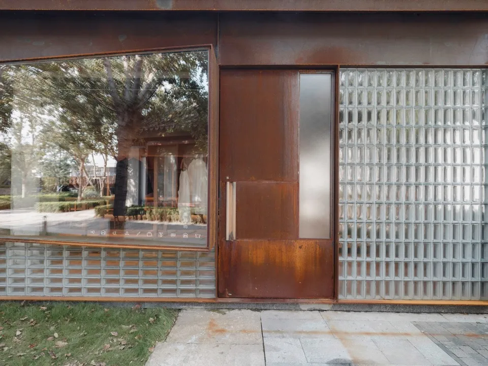 A rustic metal building exterior with a reflective window and a glass block wall.