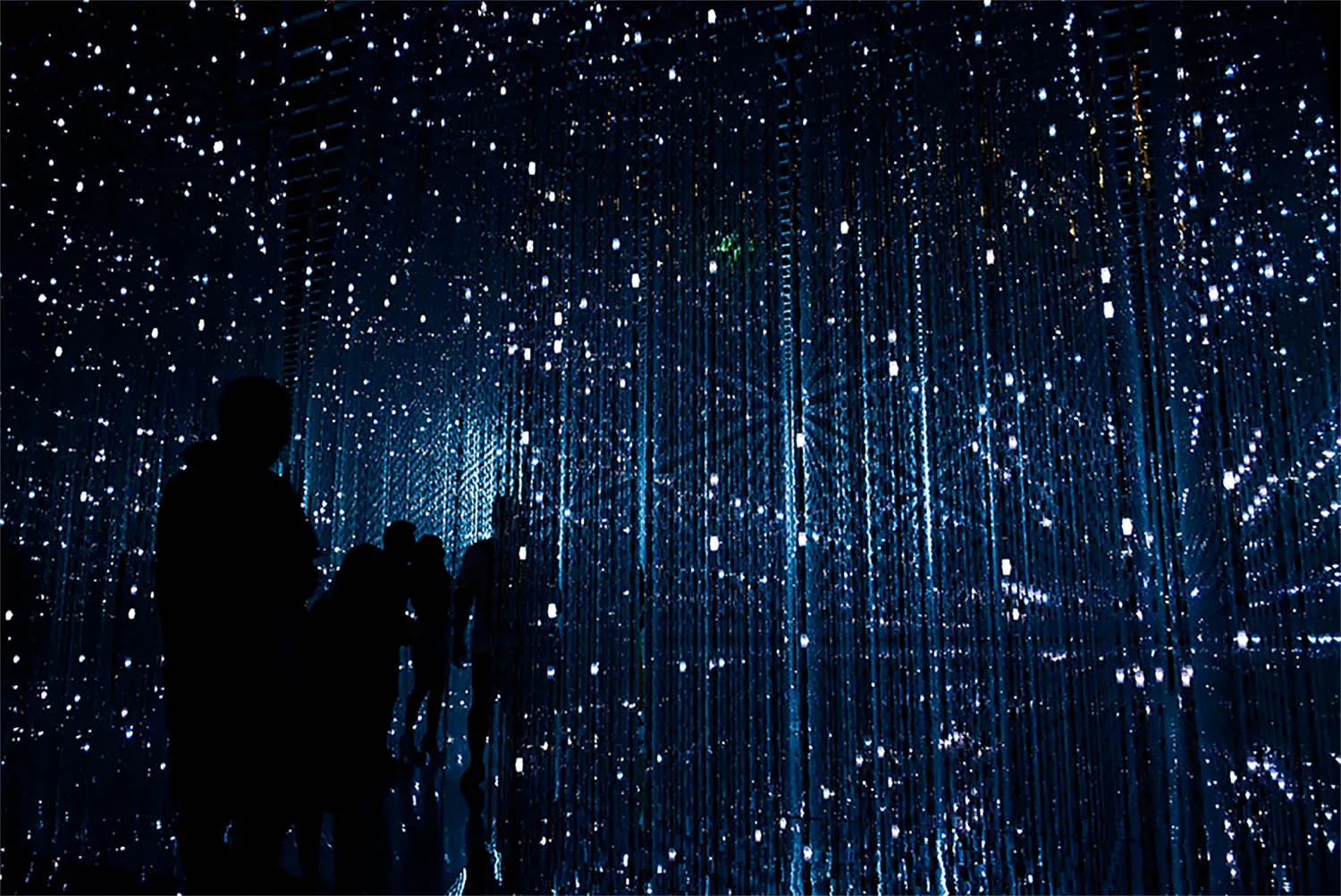 A nighttime scene featuring an interactive light installation with thousands of hanging lights suspended from the ceiling. Vi
