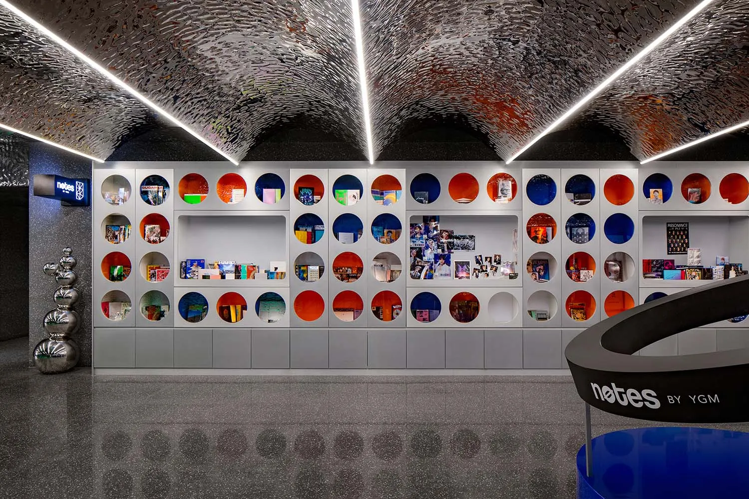 A modern bookstore with metallic surfaces and circular openings displaying books and other items.