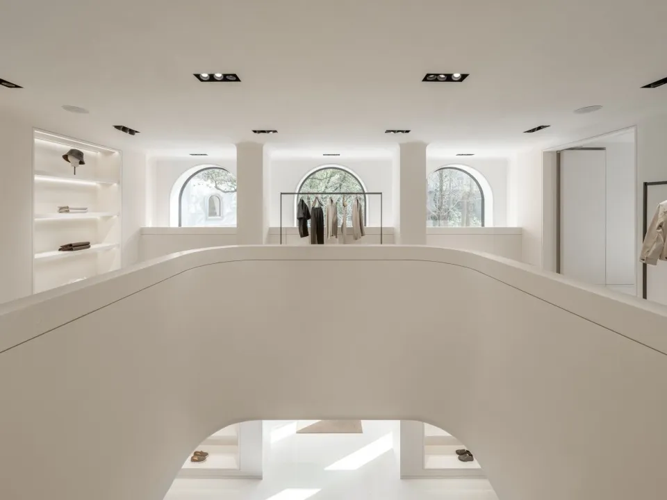 A modern retail store with minimalist design, white walls, and arched windows showcasing clothing racks and shelves.