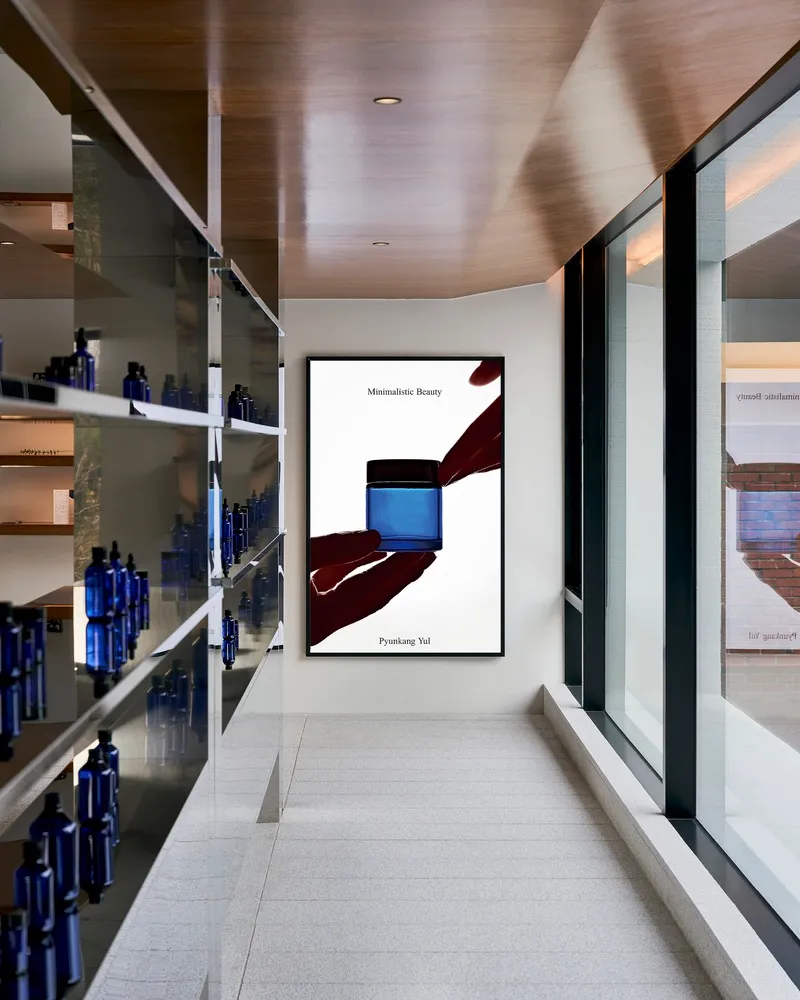 A modern minimalist interior featuring glass shelves displaying various bottles of cosmetic products.