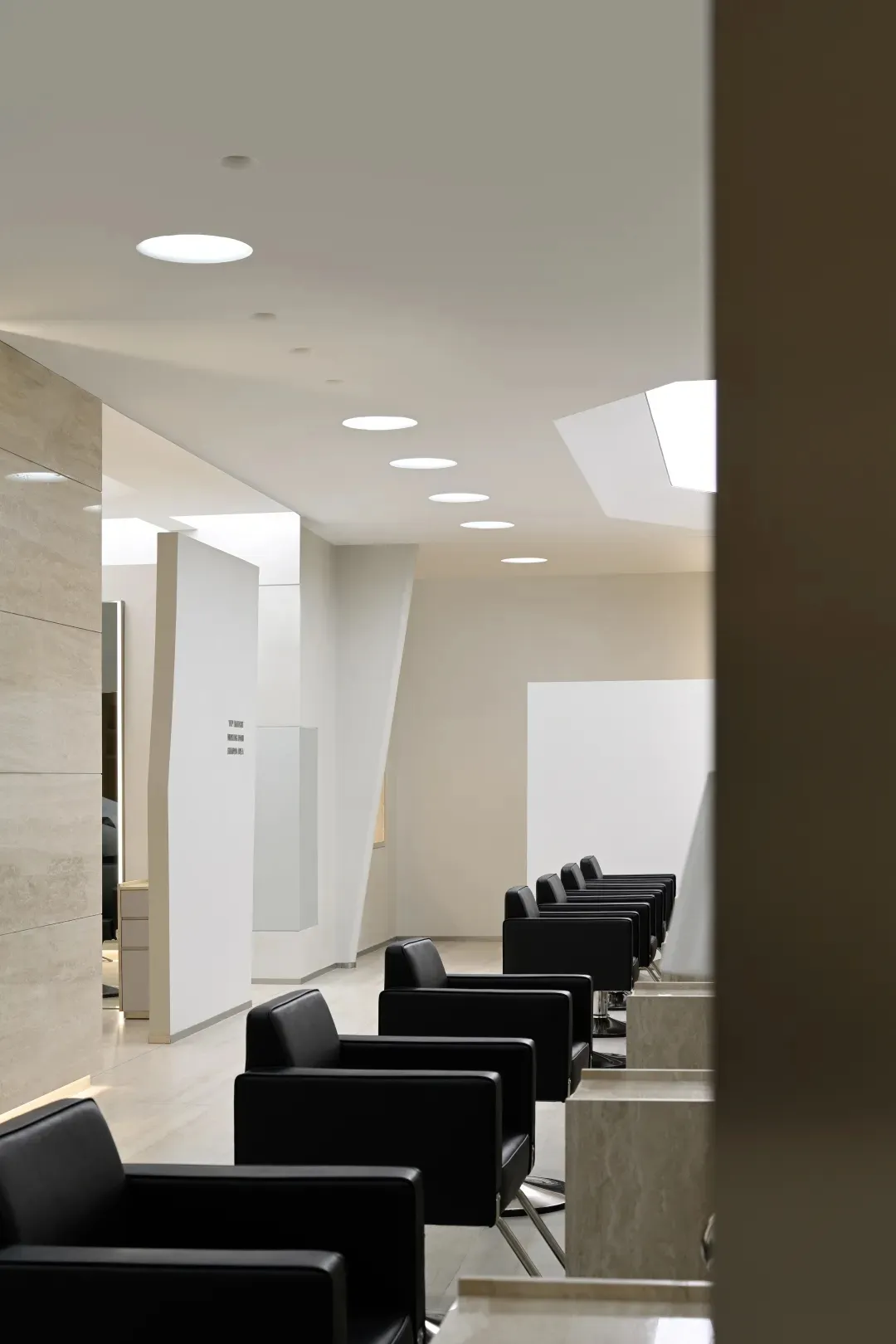 Modern salon with black leather seating, marble countertops, and glass paneling.