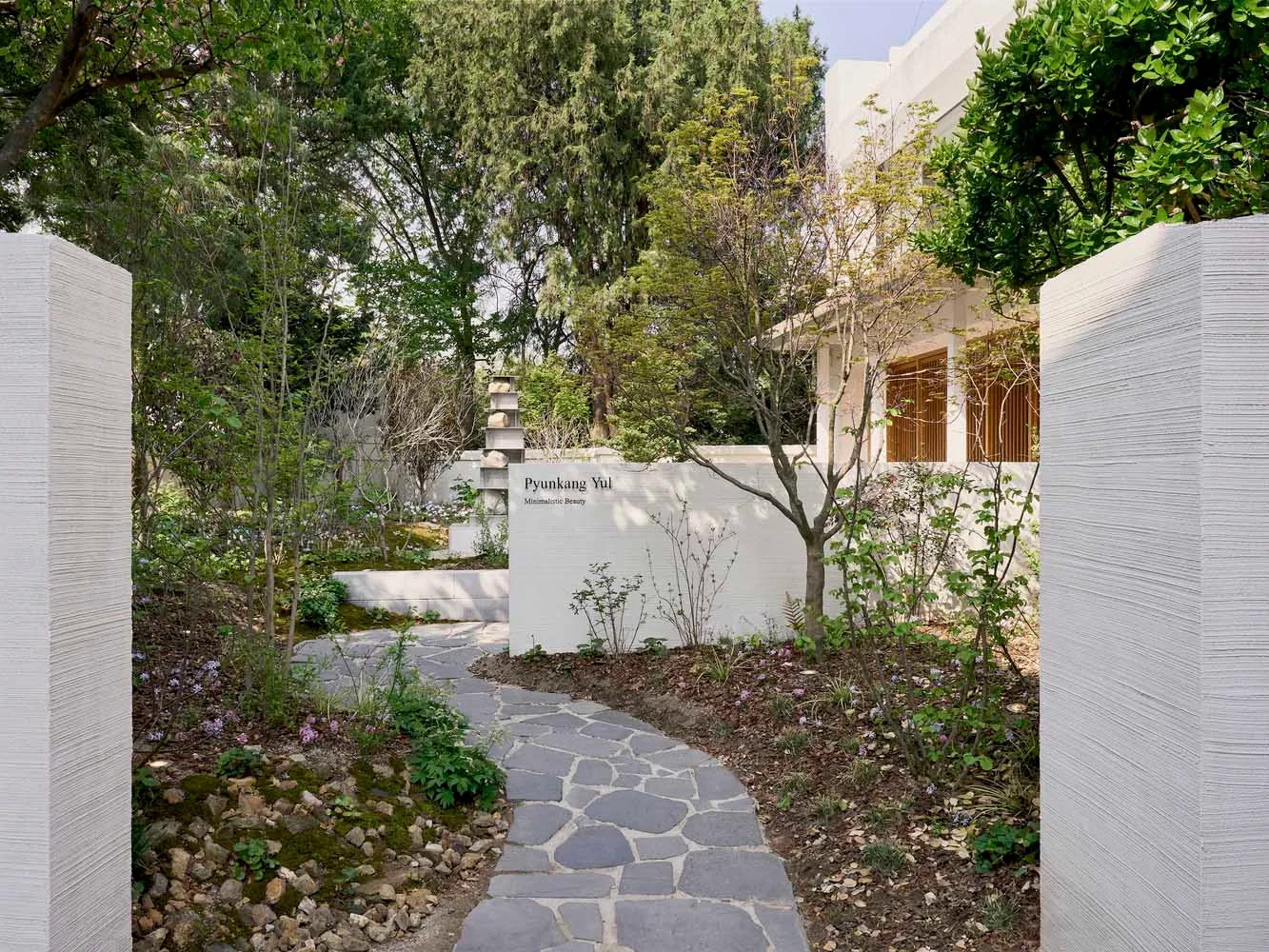 A modern garden featuring natural stones surrounded by concrete pathways and walls, surrounded by greenery and trees.