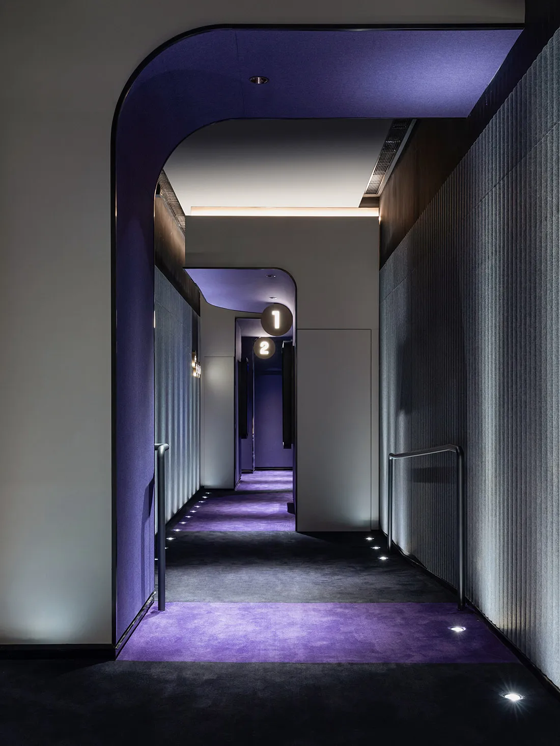 An interior photograph of a modern hotel corridor featuring minimalist design elements such as vinyl flooring and concrete co