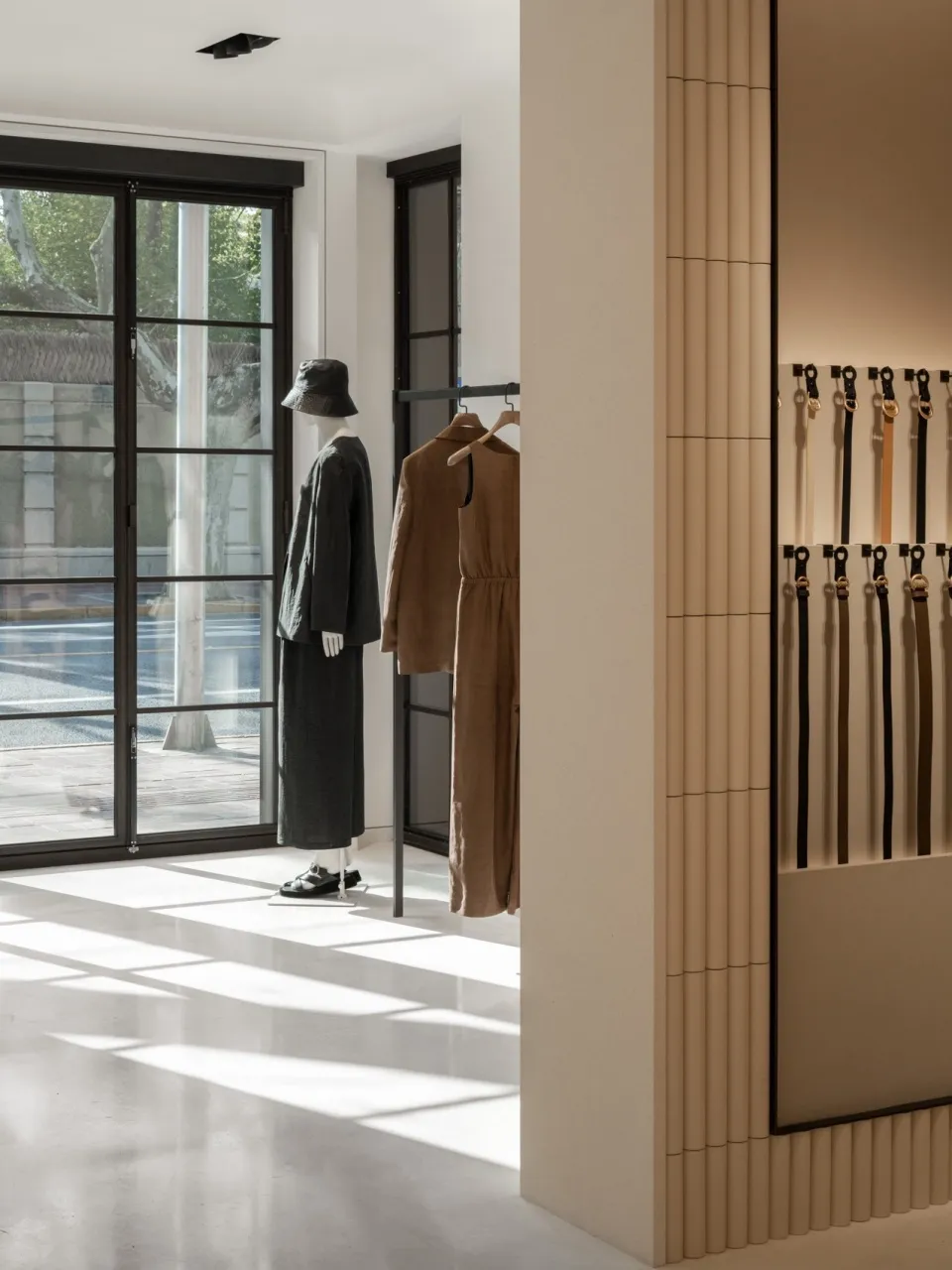 都市零售店面展示極簡服裝於人體模型上，並有皮帶整齊排列於牆面。