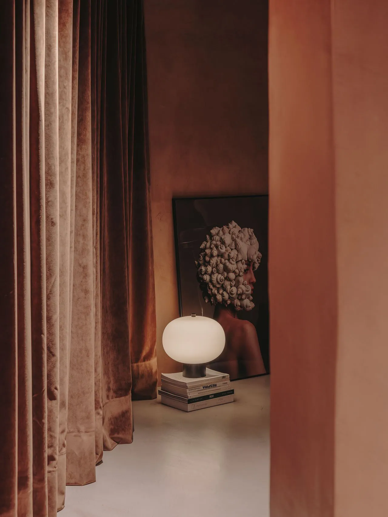 A living room with velvet curtains and a lamp on books.