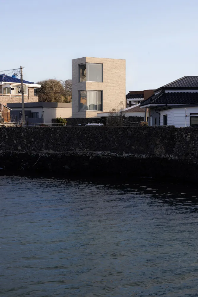 A modern brick waterfront house with a tower-like structure and large windows.