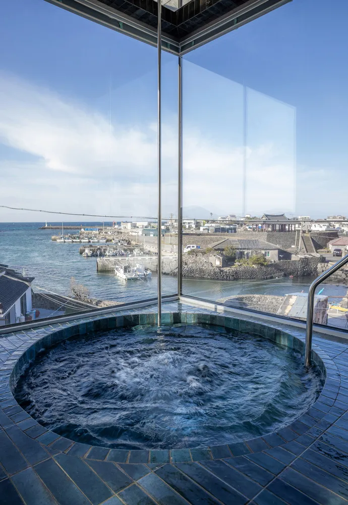 A hot tub set against a stunning coastal view, with water flowing and a clear blue sky above.