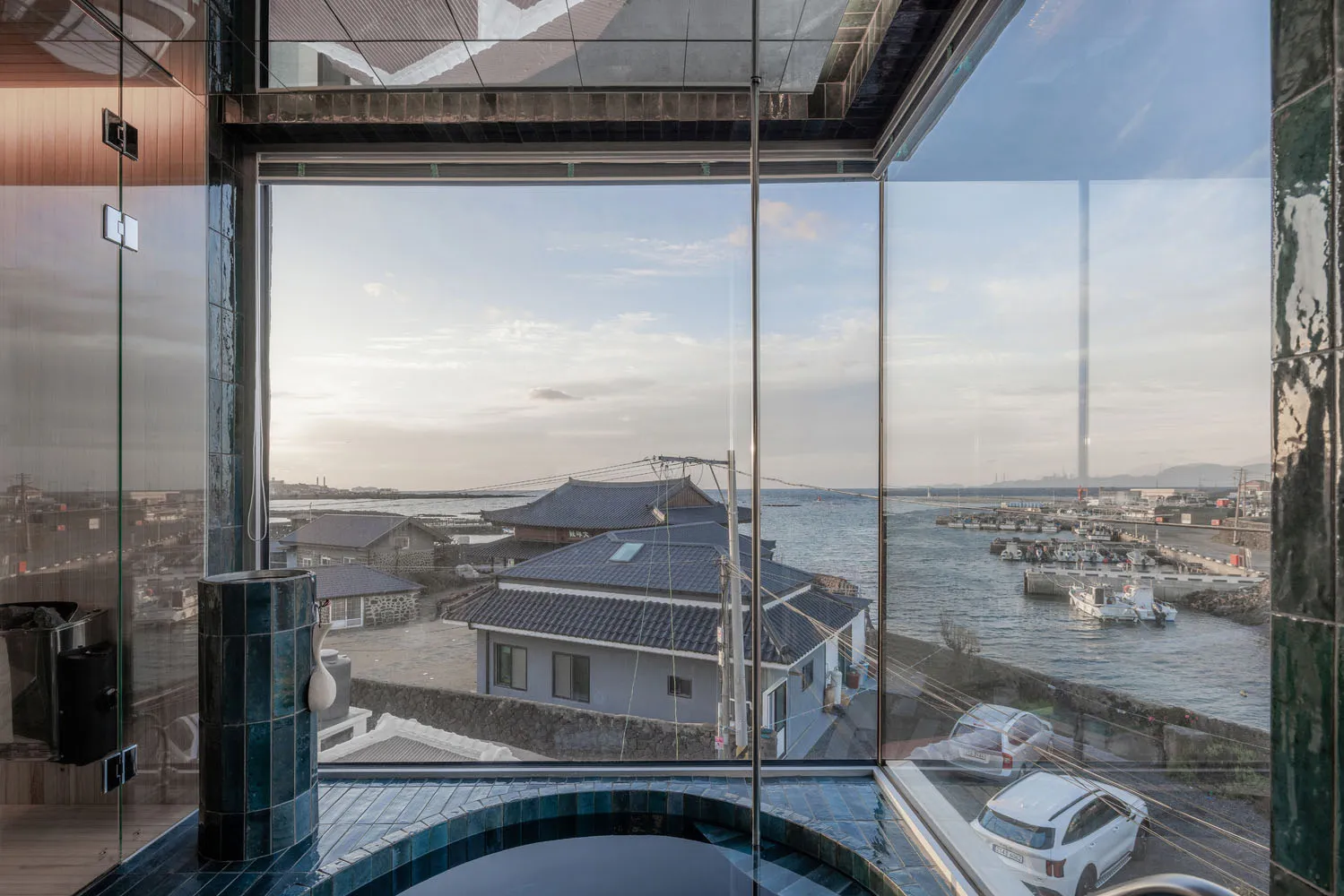 A minimalist window view of a coastal town with glass siding and blue-tiled floor.