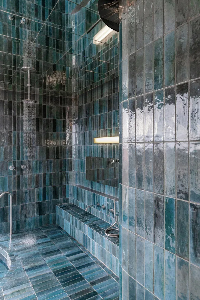 A modern bathroom with blue glass tiles covering the walls, floor, and shower area.