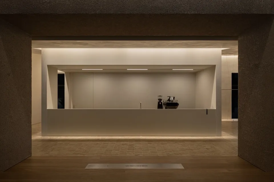A minimalist coffee shop with a concrete counter, minimal furniture, and soft lighting.