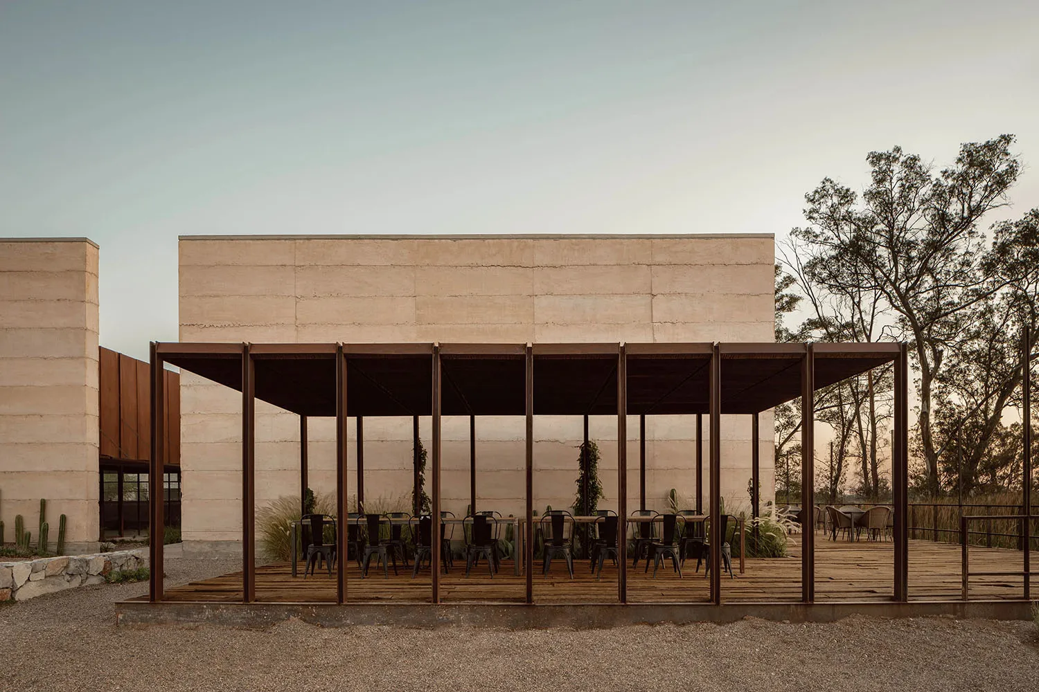 A modern cafe with metal tables and chairs, wooden flooring, and concrete walls and pillars.