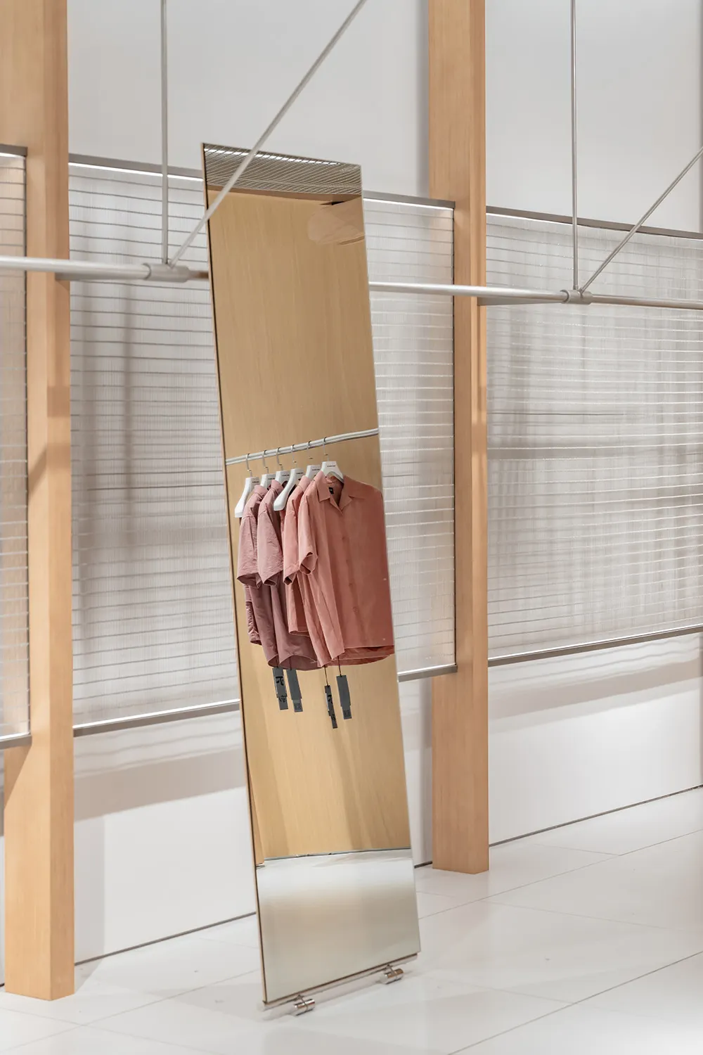 A modern hanging coat rack displaying metallic pink shirts in a minimalist retail shop setting.