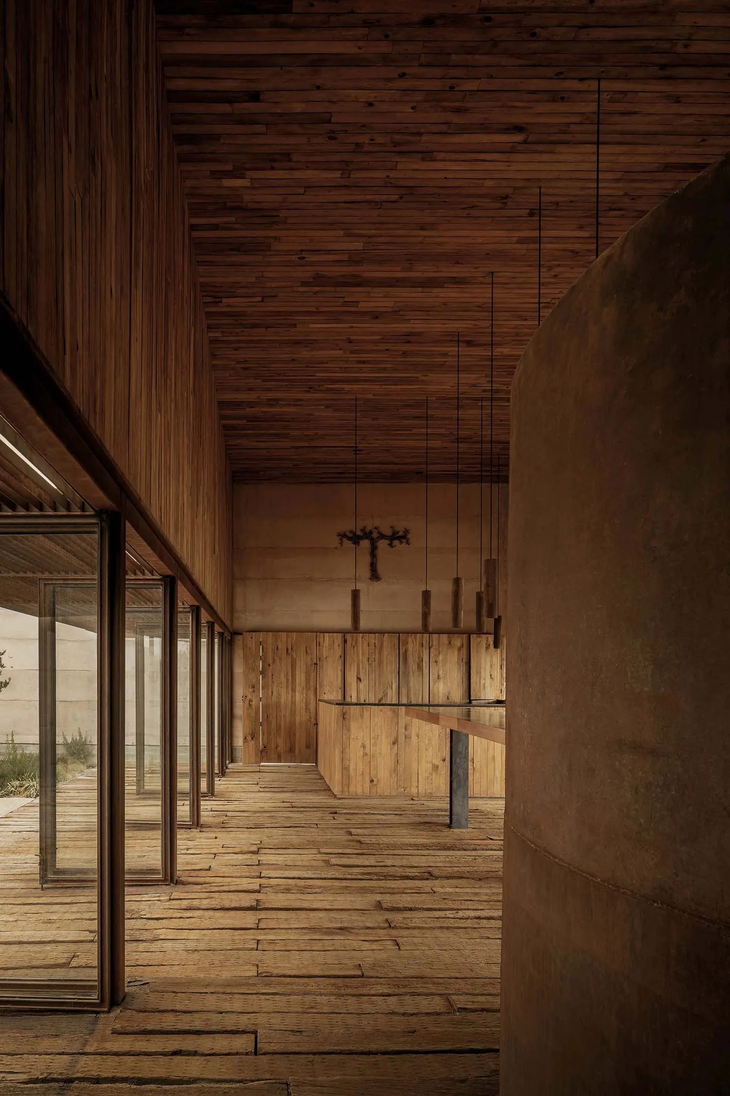 Modern living room featuring wooden paneling along the walls and ceiling, with a table in the foreground and a cross hanging