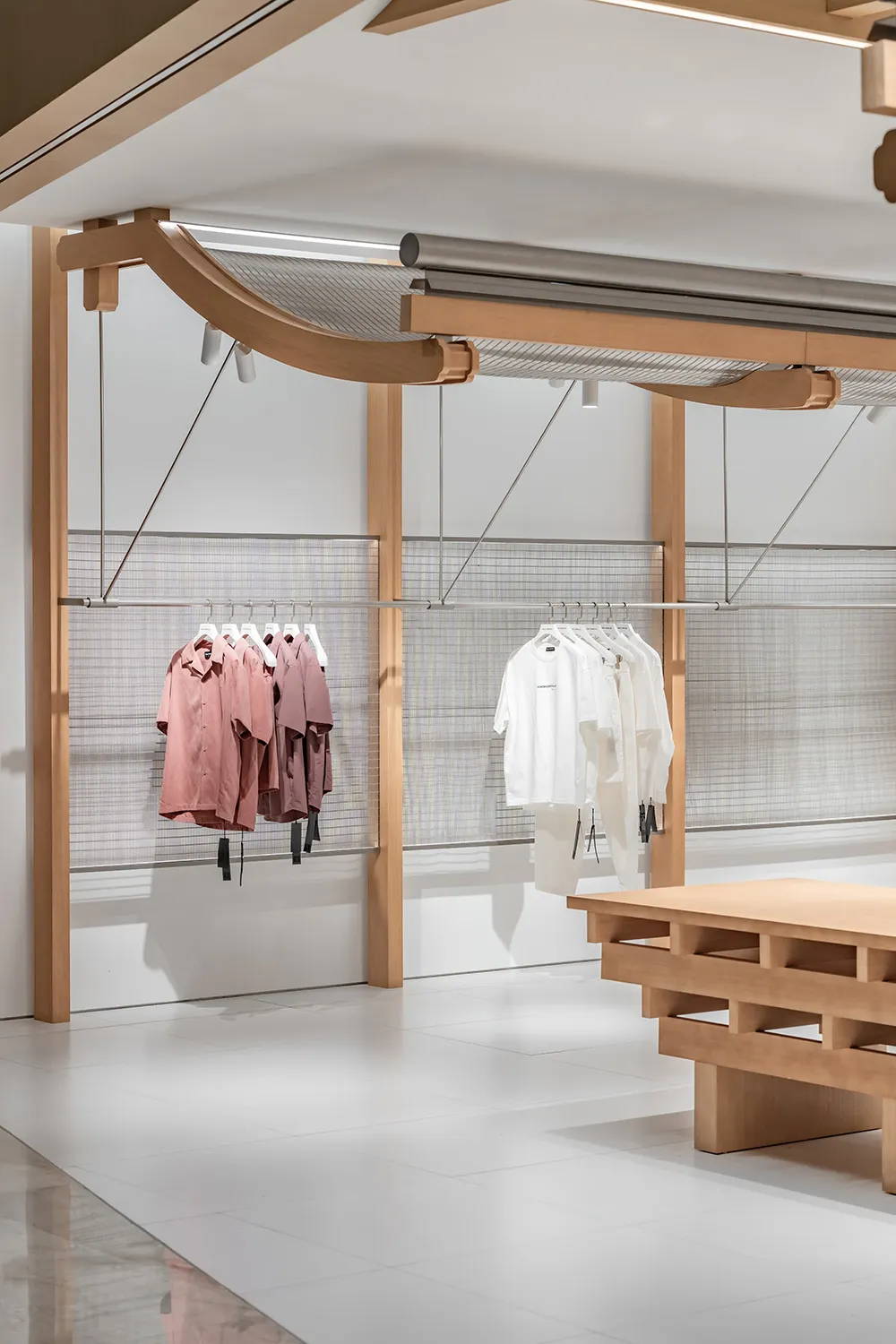 零售店內展示懸掛衣架的服裝，搭配木質橫樑與網格牆面。
