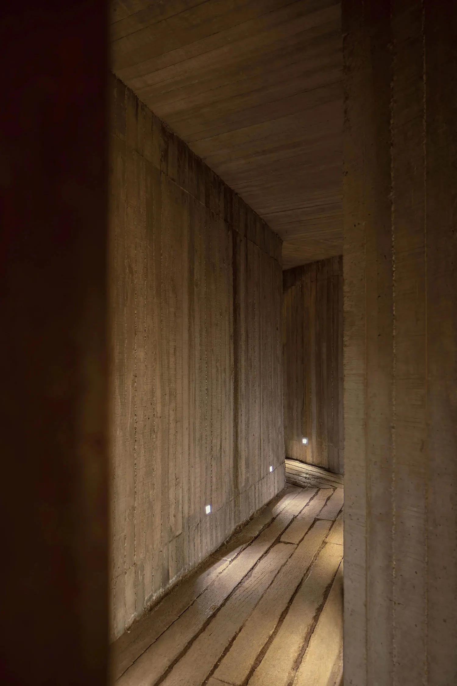 A modern corridor lined with concrete walls and illuminated by recessed lights.