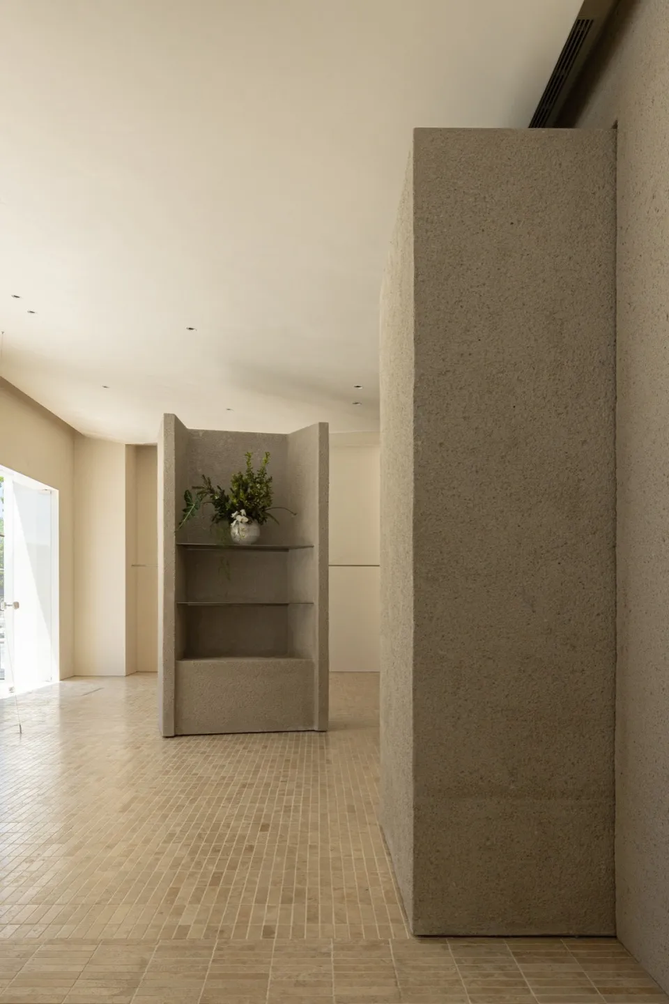 A minimalist room with concrete walls and floors, featuring a vase of flowers on a shelf.